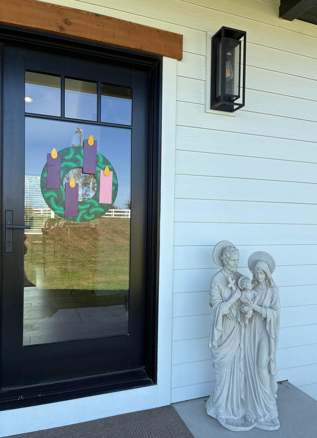 Advent wreath on a front door beside a Holy Family statue.